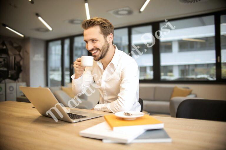 depth of field photo of man sitting on chair while holding cup in front of table